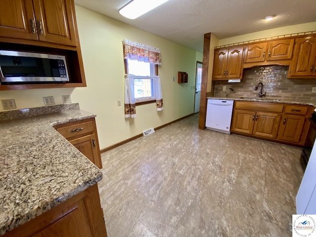 kitchen with brown cabinets, stainless steel microwave, backsplash, white dishwasher, and a sink