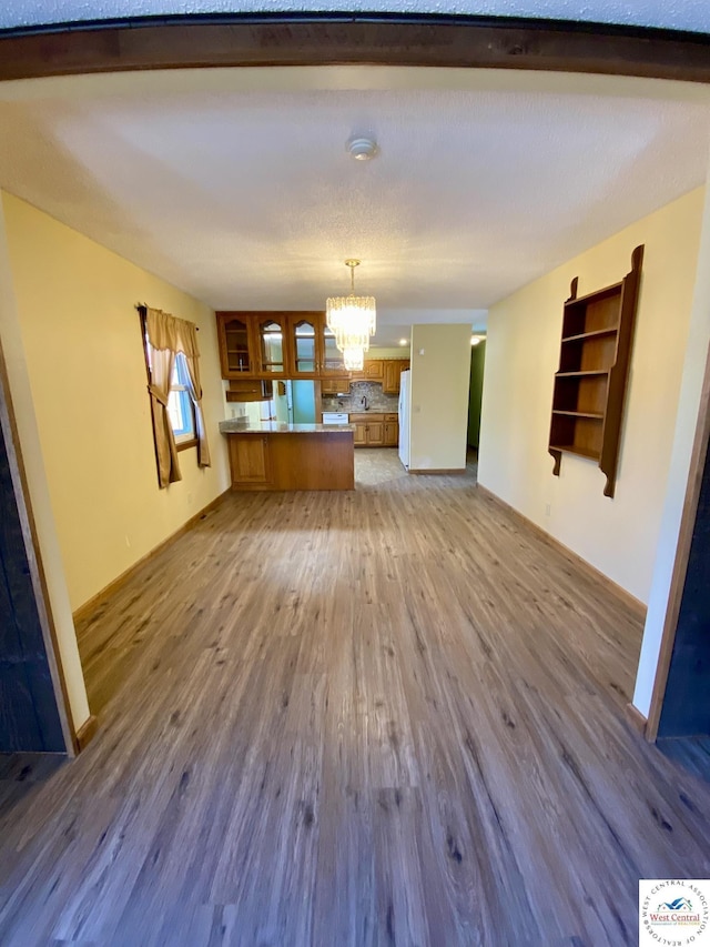 unfurnished living room with a chandelier, baseboards, and wood finished floors