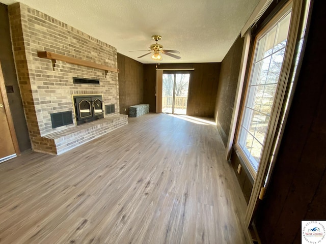 unfurnished living room with visible vents, ceiling fan, wood finished floors, a textured ceiling, and a brick fireplace