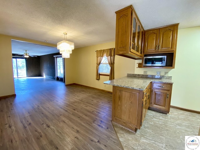 kitchen with open floor plan, light wood-type flooring, brown cabinetry, stainless steel microwave, and glass insert cabinets