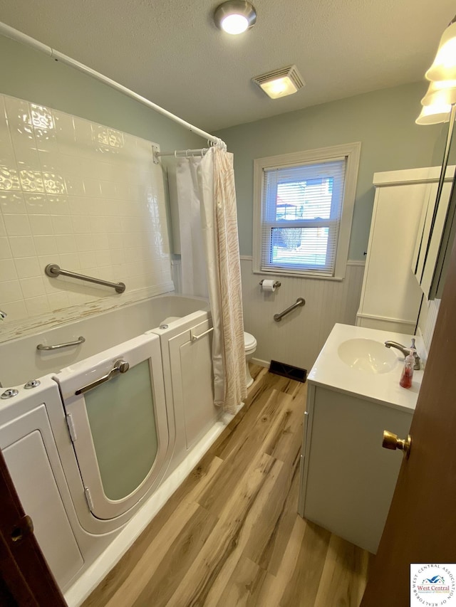 bathroom with a wainscoted wall, toilet, a textured ceiling, vanity, and wood finished floors