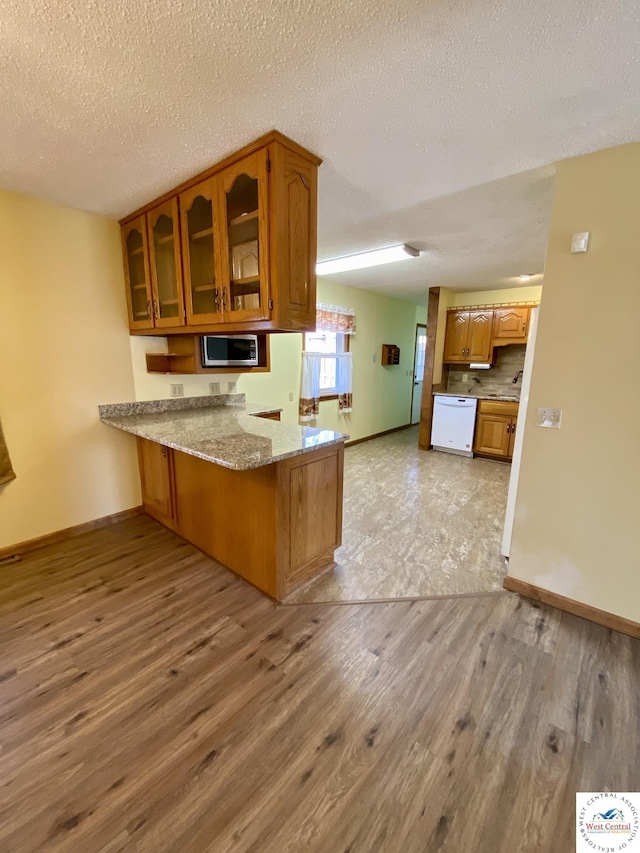 kitchen featuring stainless steel microwave, brown cabinetry, light wood-style floors, glass insert cabinets, and a peninsula