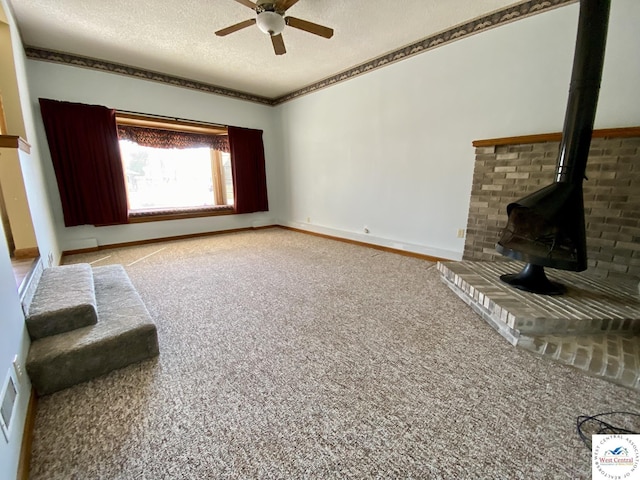 unfurnished living room featuring baseboards, ceiling fan, a wood stove, a textured ceiling, and carpet flooring