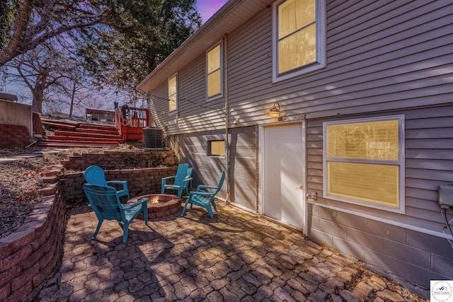 patio terrace at dusk with central AC unit, stairs, and a fire pit