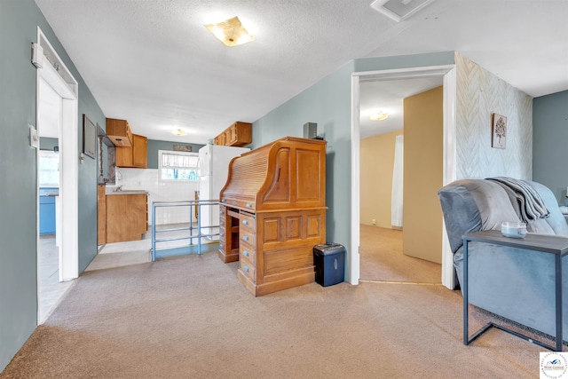 kitchen with light carpet, visible vents, brown cabinets, freestanding refrigerator, and a textured ceiling