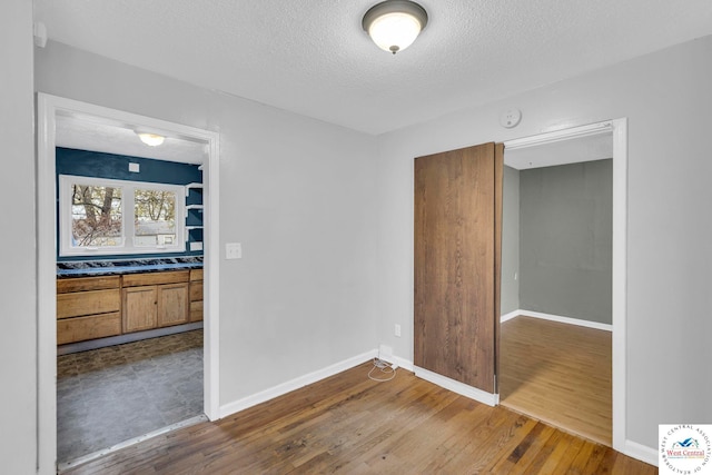 empty room featuring a textured ceiling, baseboards, and wood finished floors