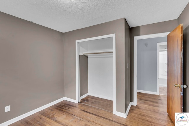 unfurnished bedroom featuring a textured ceiling, light wood finished floors, a closet, and baseboards