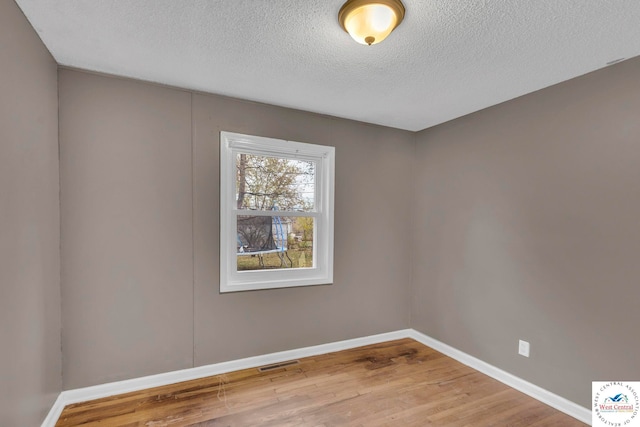 spare room featuring baseboards, a textured ceiling, visible vents, and wood finished floors