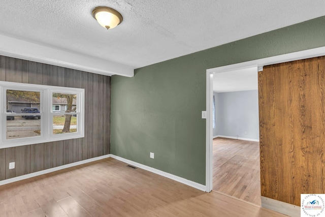 empty room with a textured ceiling, wood finished floors, visible vents, and baseboards