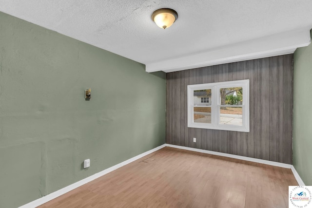 spare room with beamed ceiling, a textured ceiling, baseboards, and wood finished floors