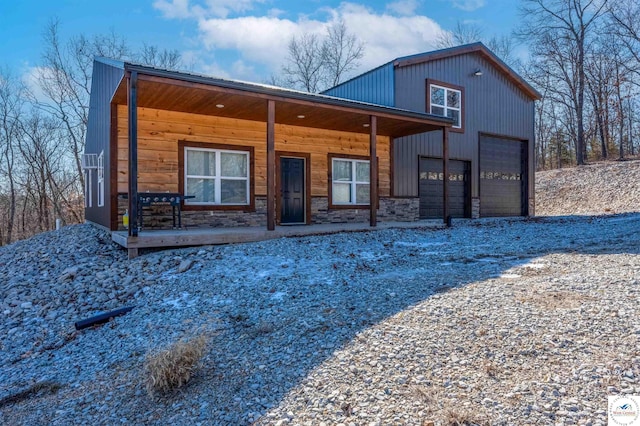 back of house with gravel driveway, stone siding, a garage, and a porch