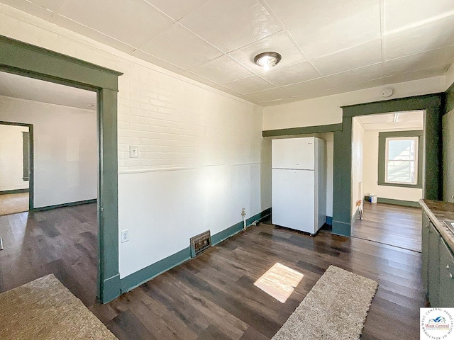 empty room featuring a drop ceiling, dark wood finished floors, and baseboards