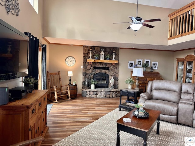 living room featuring a towering ceiling, ceiling fan, a fireplace, and wood finished floors