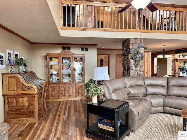 living area with visible vents, ceiling fan, ornamental molding, wood finished floors, and a textured ceiling