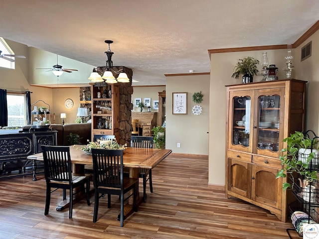 dining room featuring ornamental molding, a stone fireplace, wood finished floors, and visible vents