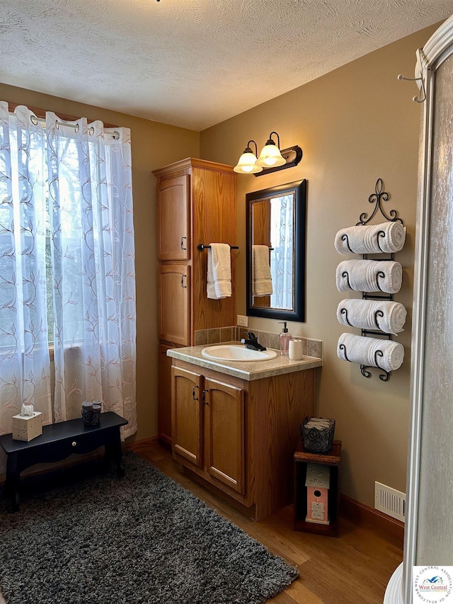 bathroom featuring a textured ceiling, wood finished floors, vanity, visible vents, and baseboards