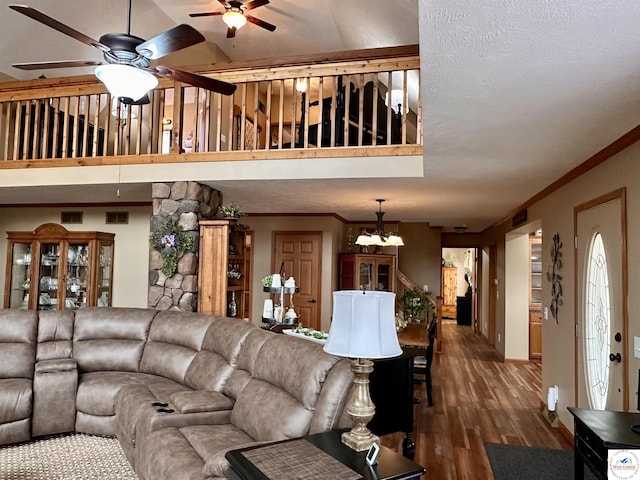 living room with ceiling fan with notable chandelier, ornamental molding, wood finished floors, and a high ceiling