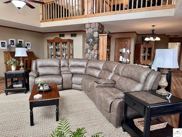 living room featuring wood finished floors, crown molding, a towering ceiling, and ceiling fan with notable chandelier