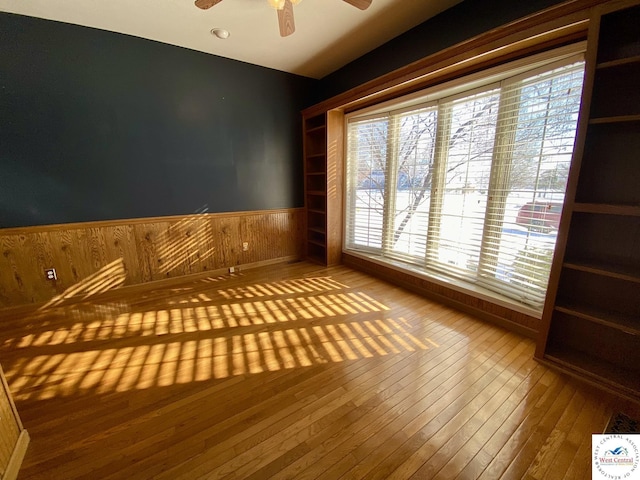 spare room with a wainscoted wall, ceiling fan, and wood finished floors