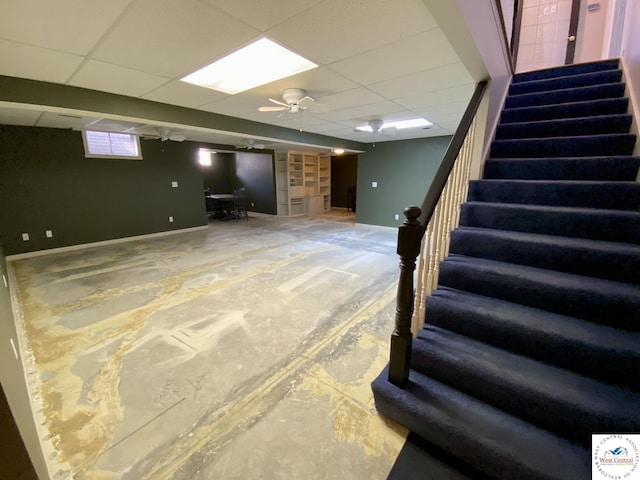 basement featuring a ceiling fan, a paneled ceiling, baseboards, and stairs