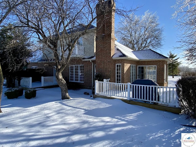 snow covered rear of property featuring brick siding and a chimney