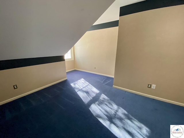 additional living space featuring dark carpet, baseboards, and vaulted ceiling