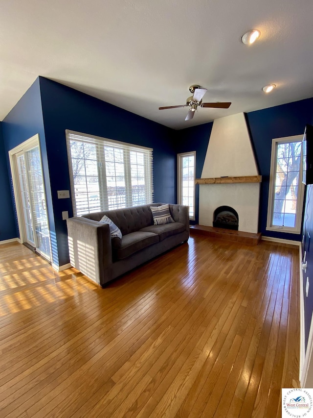 unfurnished living room with a large fireplace, a ceiling fan, baseboards, and wood finished floors