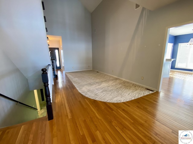 unfurnished living room with light wood-style floors, visible vents, a towering ceiling, and baseboards