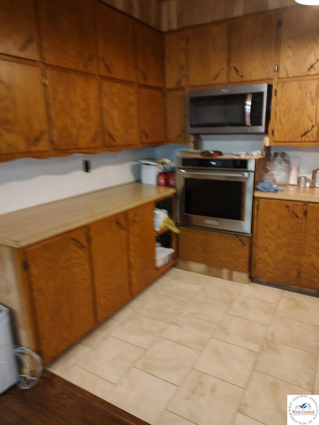 kitchen with appliances with stainless steel finishes, brown cabinets, light countertops, and light tile patterned floors