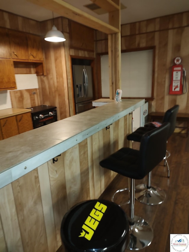 kitchen with wooden walls, light countertops, stainless steel refrigerator with ice dispenser, dark wood-style floors, and pendant lighting