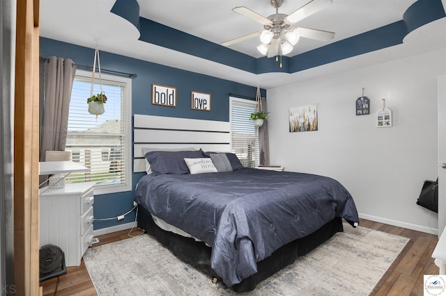 bedroom featuring ceiling fan, a tray ceiling, baseboards, and hardwood / wood-style floors