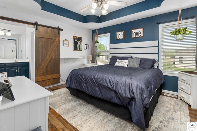 bedroom with a tray ceiling, a barn door, baseboards, and wood finished floors