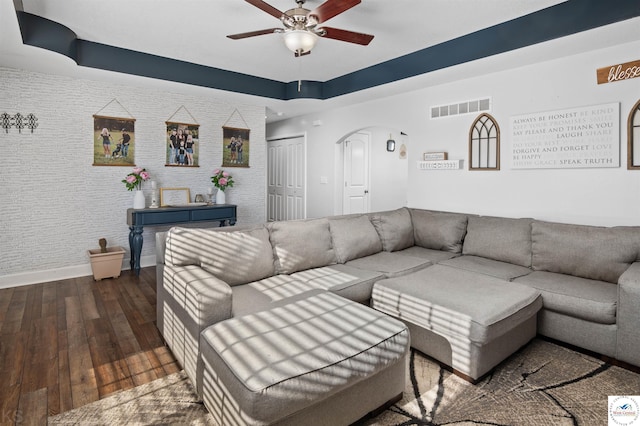 living room with visible vents, a ceiling fan, arched walkways, wood-type flooring, and a raised ceiling