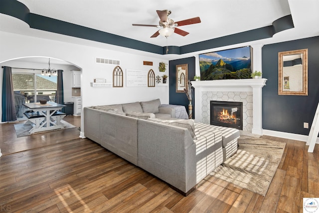 living room with hardwood / wood-style floors, visible vents, a fireplace, arched walkways, and ceiling fan with notable chandelier