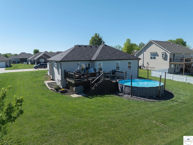 rear view of property featuring a deck, fence, a fenced in pool, and a lawn