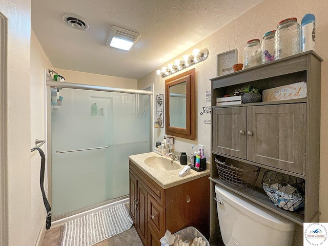 bathroom with a textured ceiling, toilet, vanity, visible vents, and a stall shower