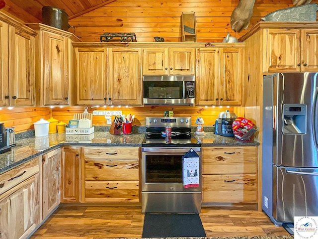 kitchen with lofted ceiling, wooden walls, appliances with stainless steel finishes, and dark stone counters