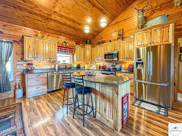 kitchen with pendant lighting, light wood finished floors, appliances with stainless steel finishes, a kitchen island, and dark stone countertops