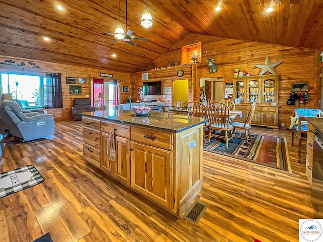 kitchen featuring wood walls, dark stone counters, open floor plan, and decorative light fixtures