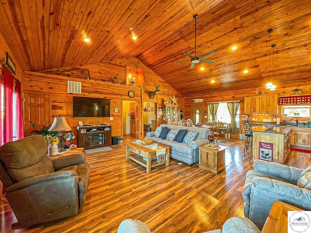 living room with visible vents, wood walls, wood finished floors, high vaulted ceiling, and wooden ceiling