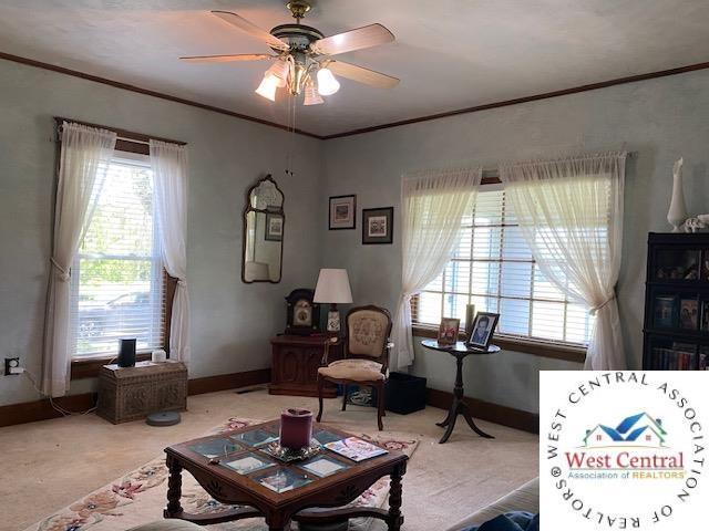 living room featuring baseboards, carpet, a ceiling fan, and crown molding