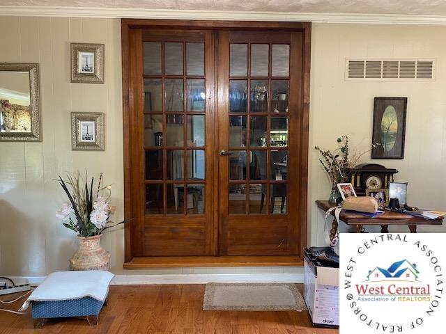 doorway to outside featuring visible vents, wood finished floors, and ornamental molding