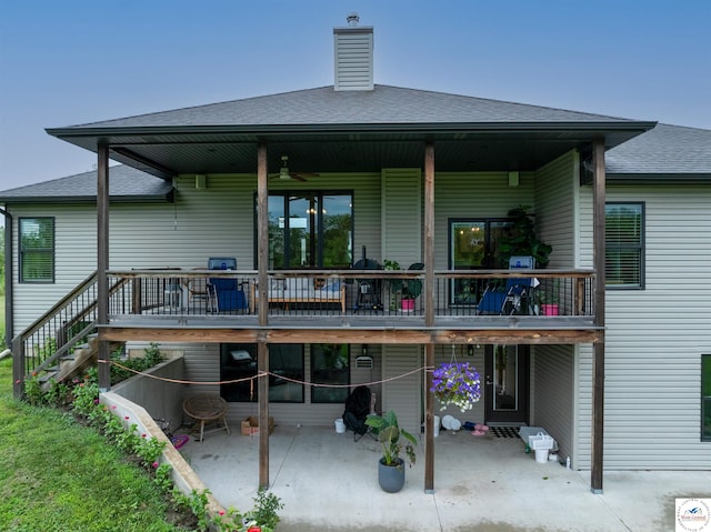 rear view of house with roof with shingles, a patio, a chimney, a wooden deck, and stairs