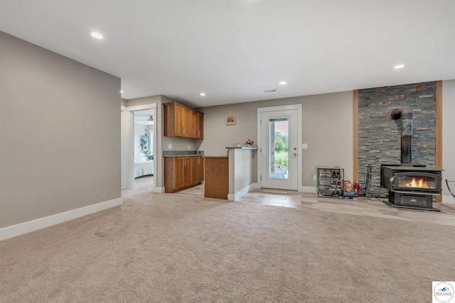 kitchen with light carpet, baseboards, brown cabinets, open floor plan, and a wood stove