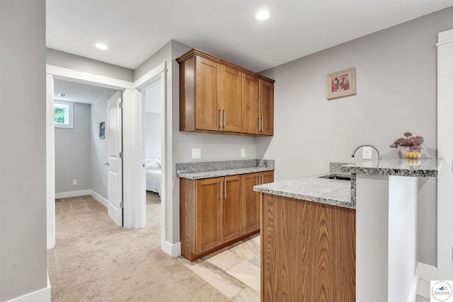 kitchen featuring brown cabinets, a sink, light carpet, and a peninsula