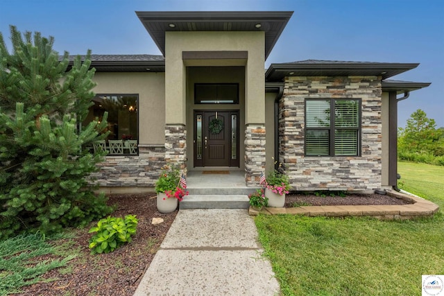 entrance to property featuring stone siding, a yard, and stucco siding