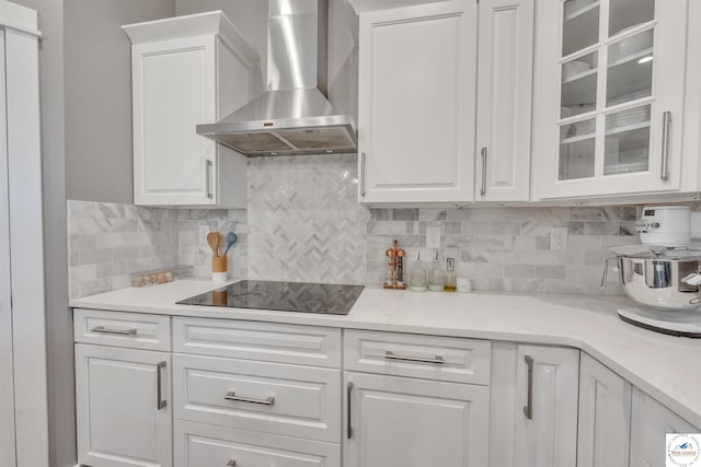 kitchen with glass insert cabinets, wall chimney range hood, and white cabinetry