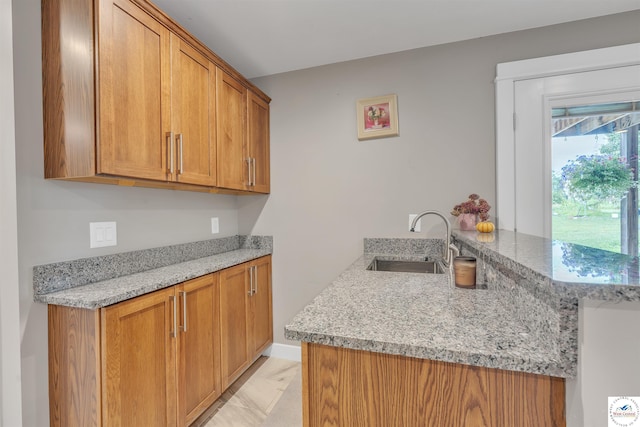 kitchen featuring marble finish floor, brown cabinets, a sink, light stone countertops, and a peninsula