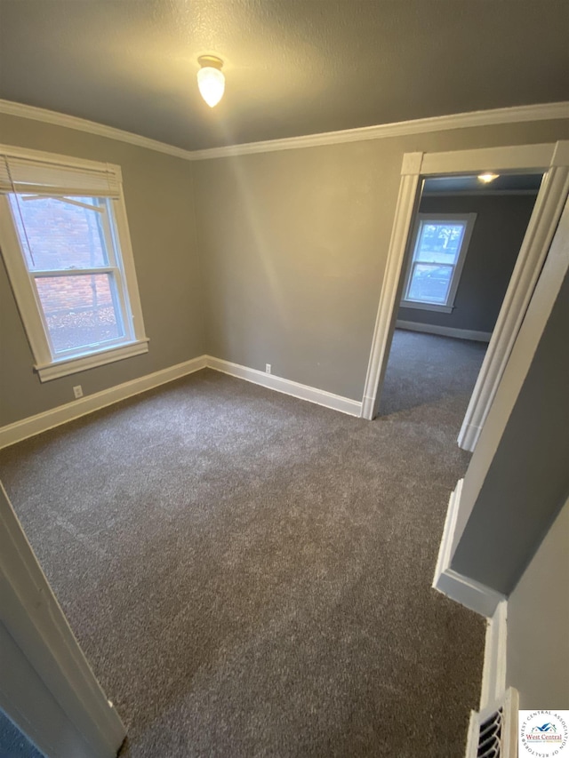 spare room with a wealth of natural light, dark colored carpet, crown molding, and baseboards