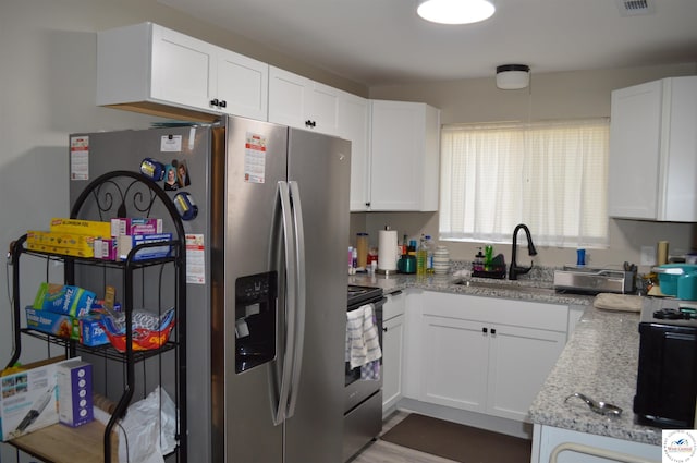 kitchen featuring electric range, white cabinetry, stainless steel refrigerator with ice dispenser, and a sink